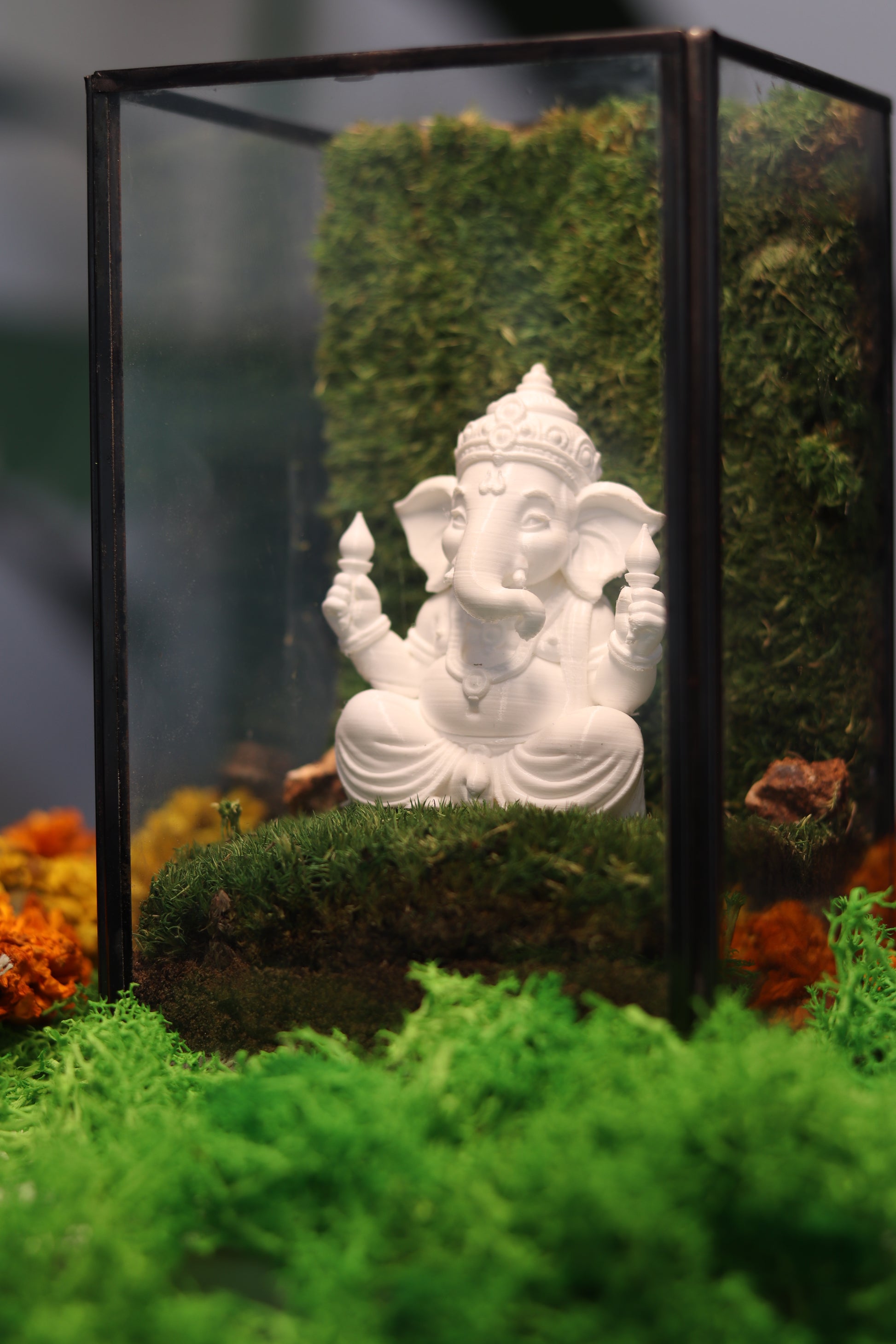 White statue in a glass display case with green moss and orange flowers